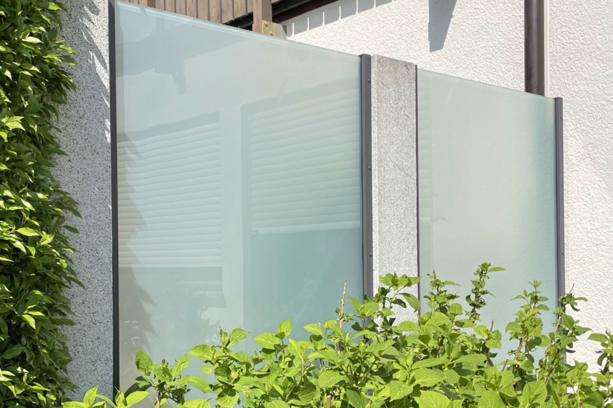 Sichtschutzzaun mit Glaselementen umrandet von grüner Vegetation als Beispiel unserer Leistungen.