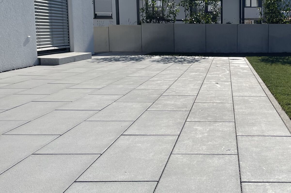 Sicht auf eine Terrasse mit hellgrauuen Feinsteinzeugplatten als Beispiel unserer Leistungen.