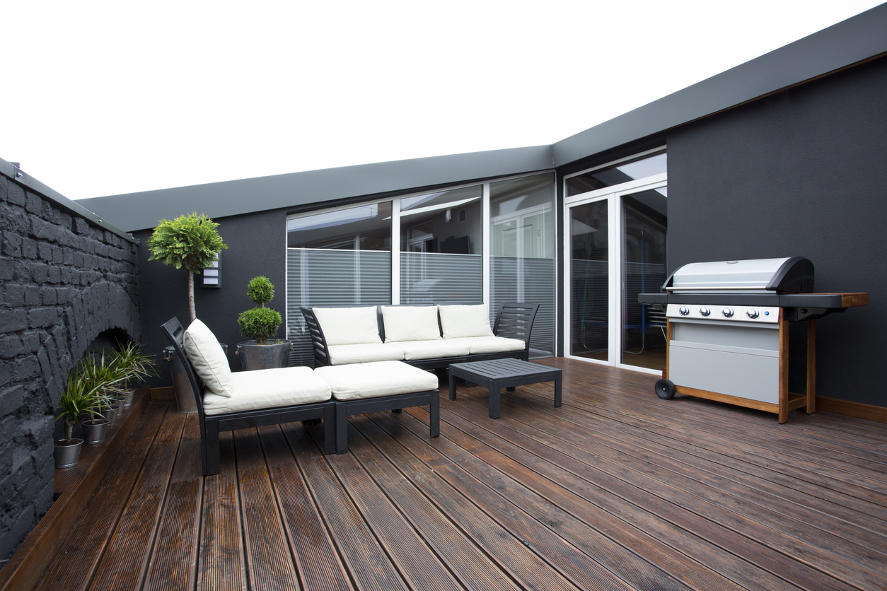 Terrassen- und Wegebau: Loggia mit Terasse aus dunklem Holz mit Loungemöbel und Grill vor Fenstern und Terassentür