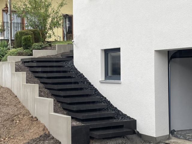 schwebende Treppe mit dunkelgrauen Betonplatten zum Hauseingang