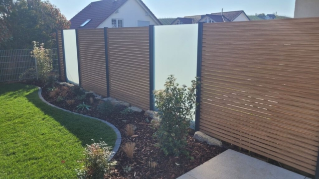 Sichtschutz ALU Rhombus mit Glaselementen als Abgrenzung zum Nacbarn. Im Vordergrund ein Pflanzbeet, abgrtrennt von einem Einzeiler zum Rollrasen.