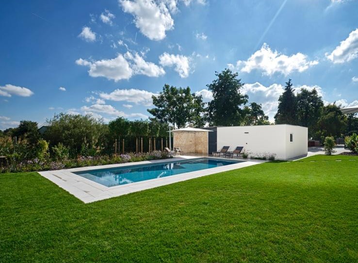 GFK-Pool: einteiliges Becken aus glasfaserverstärktem Kunststoff in Hellgrau, am Rand des Lochs eine weiße Folie und einige Steinplatten, im Hintergrund dunkelbrauner Holzzaun
