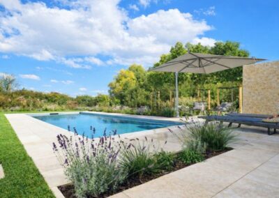 Exklusive Poolanlage mit Natursteinplatten, moderner Pergola, Bepflanzung und weitem Ausblick ins Grüne