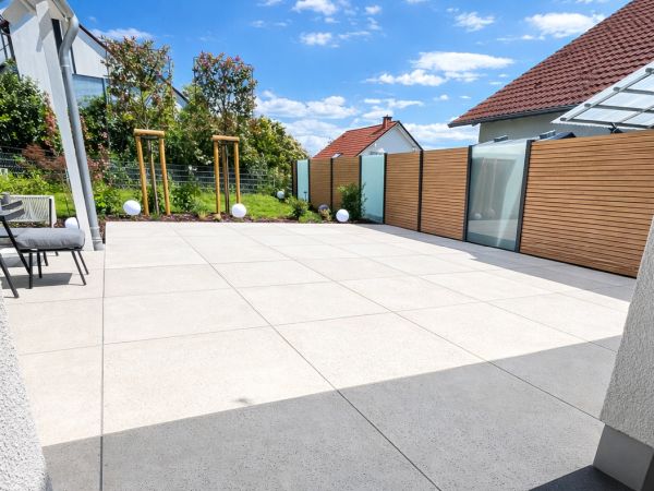 Umgestaltung & Weiterentwicklung von Außenanlagen Modern gestaltete Terrasse mit großformatigen hellen Platten, Sichtschutzelementen und angrenzendem Gartenbereich