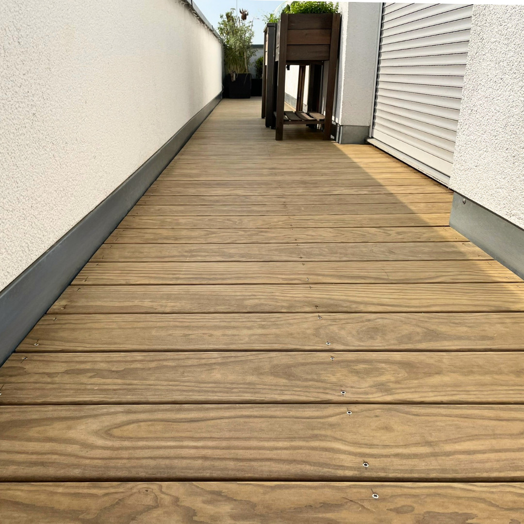 Holzterrasse für natürliche Wärme Schmale Holzterrasse zwischen zwei Hauswänden mit sichtbarer Holzmaserung, sauberer Verschraubung und Pflanzkübeln im Hintergrund