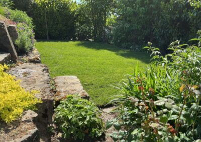 Gepflegter grüner Garten mit Rasenfläche, Natursteinmauer und blühenden Pflanzen im Sonnenlicht