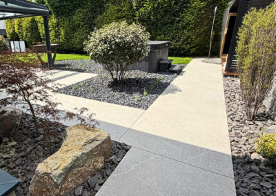 Moderner Gartenweg mit großformatigen grauen Platten, Kiesflächen, Formgehölzen, Findling, Sauna und Whirlpool im Garten