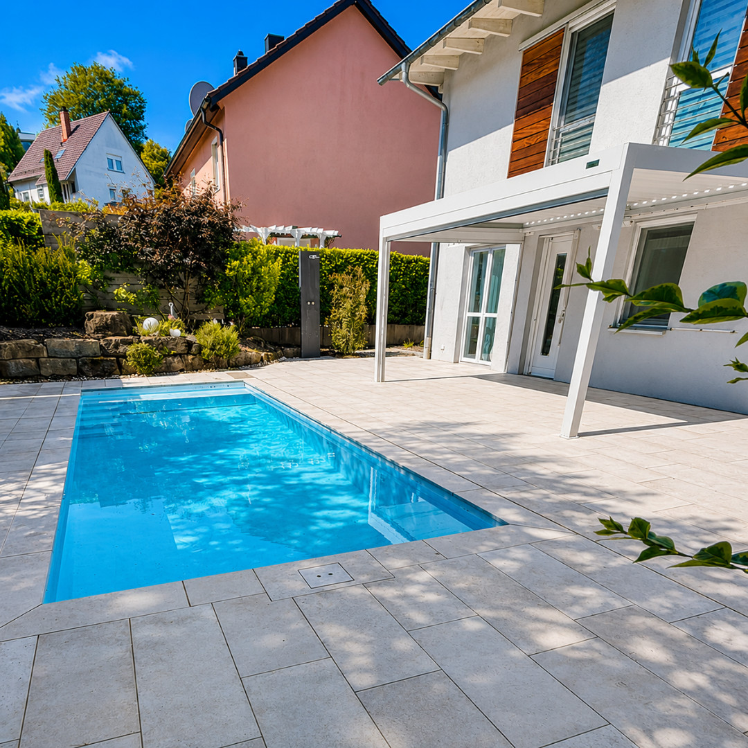 Neuanlage hochwertiger Poolgarten Moderner Poolbereich mit heller Terrassenfläche, weißer Überdachung, Wohnhaus und bepflanztem Gartenumfeld