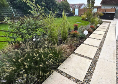 Moderner Gartenweg mit großformatigen Platten, Kiesfugen, Gräsern, Stauden, Rasenfläche und Gartenbeleuchtung