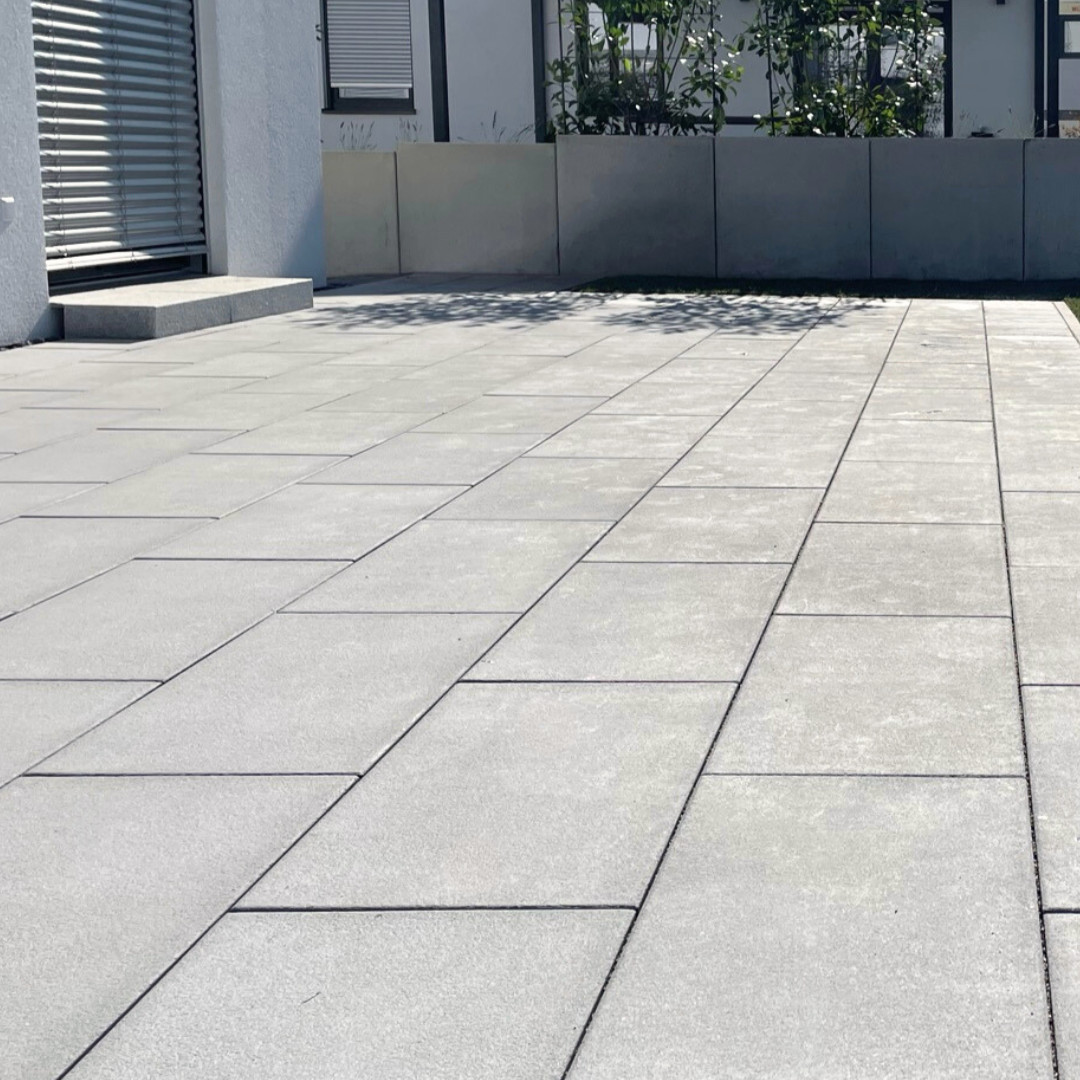 Klare Fläche für moderne Außenräume Großzügige Terrasse mit grauen Platten, klarer Verlegung und moderner Einfassung am Wohnhaus